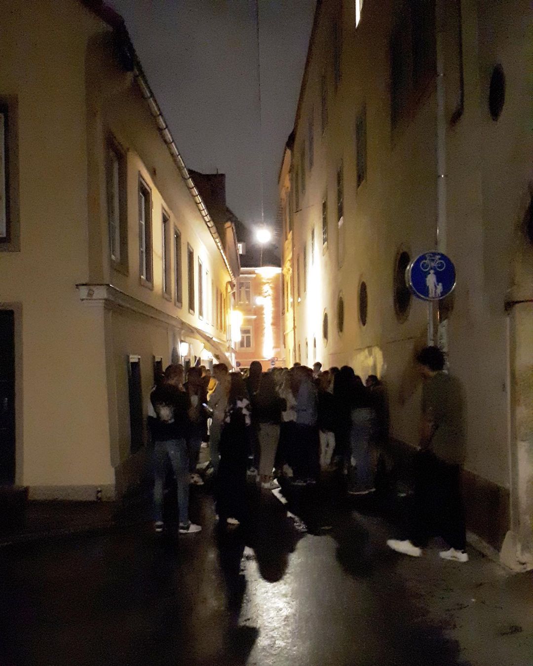 Eine Gasse in der Grazer Innenstadt am Abend. Es ist dunkel und mit einigen Lichtern aufgehängt zwischen den Gebäuden erkennt man die Umrisse vieler junger Menschen vor einer Lokalität.