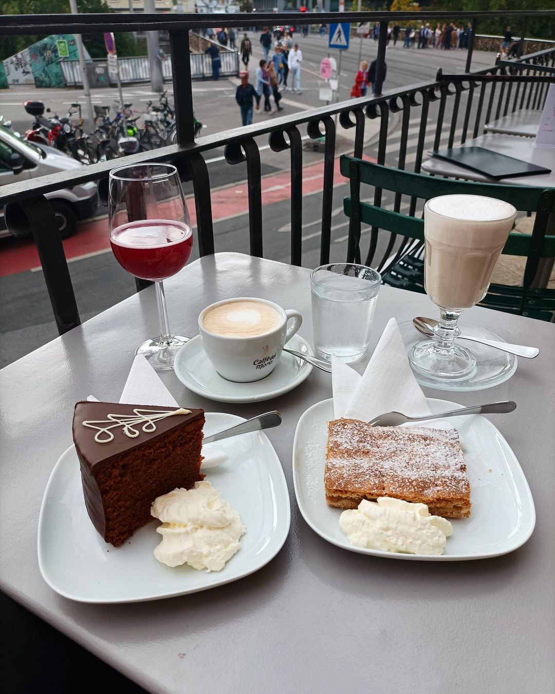 Kaffe und Kuchen im Café Schwalbennest. Ein Wein, genannt Sturm, Schokoladenkuchen und heißer Kakao und Waffeln mit Sahne auf einem kleinen Tisch im Freien.