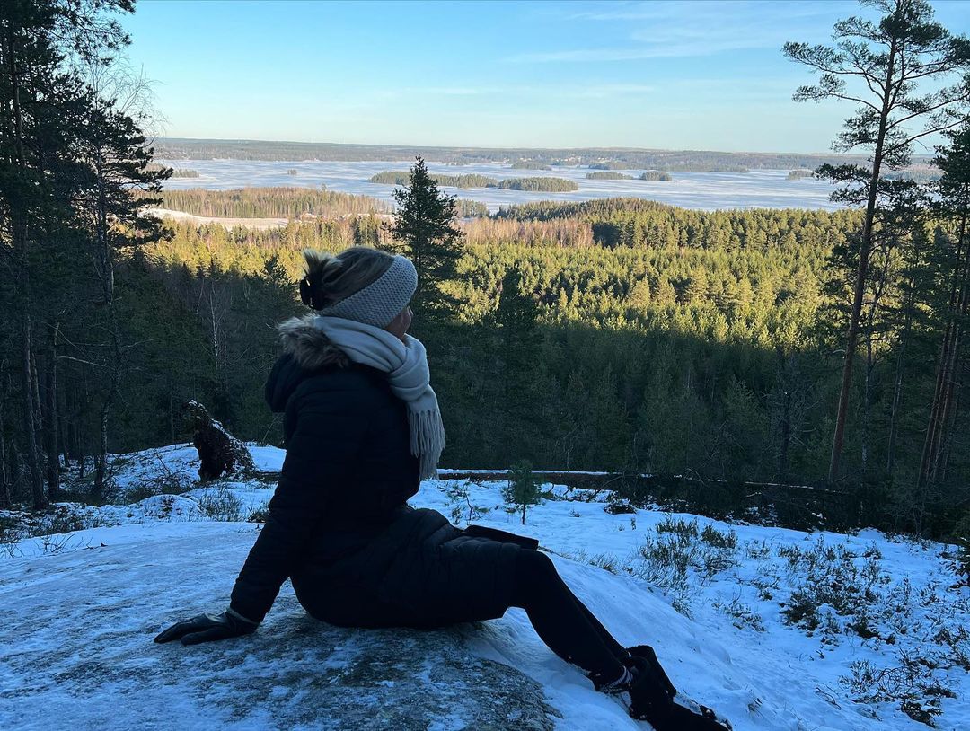 Emely sitzt warm eingepackt mit Schal und Mütze auf einem verschneiten Berg in Schweden  mit toller Aussicht