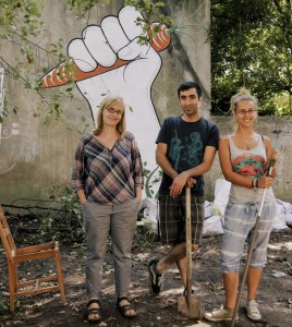 Ein Mann und zwei Frauen stehen vor einem Grafitti, dass sich in einem Garten befindet.