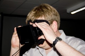Ein Mann in grauem Hemd hält sich eine VR-Brille vor die Augen.