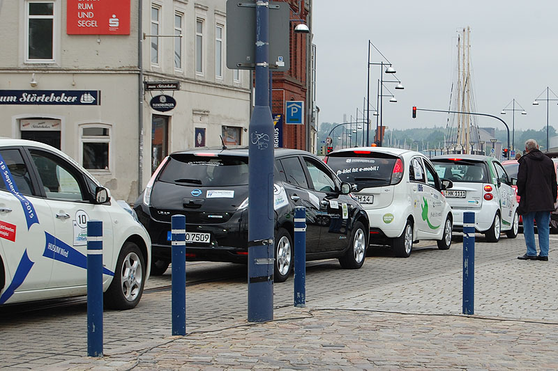 Mehrere kleine E-Autos reihen sich auf einer öffentlichen Straße aneinander.