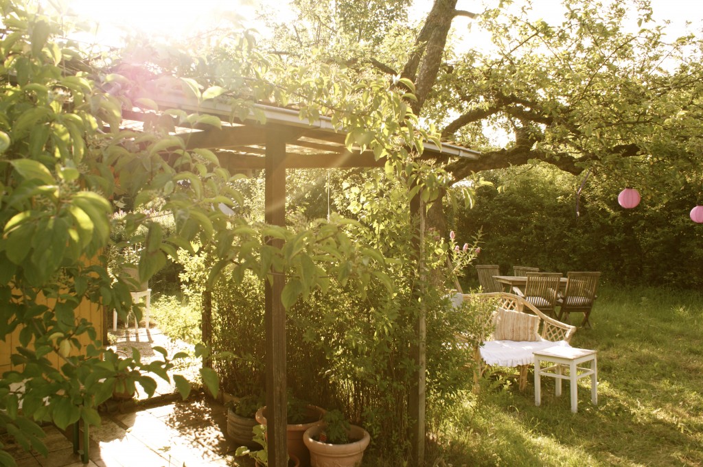 Ein schöner grüner Garten, mit einer gemütlichen Sitzecke und einem Balkendach.
