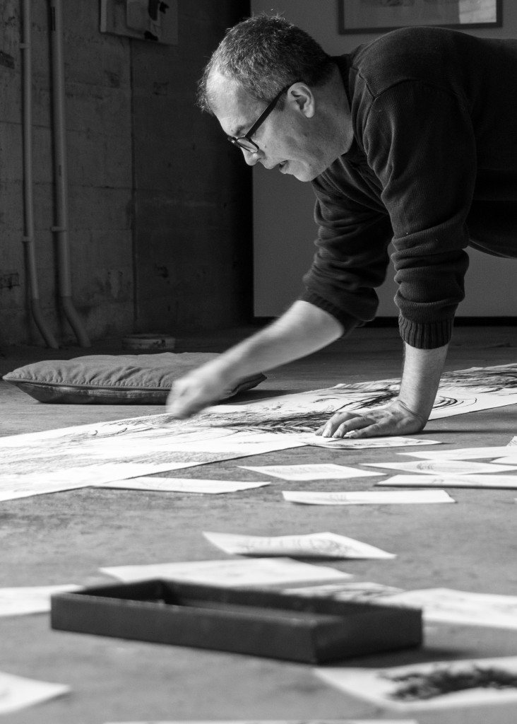 Das Schwarz-Weiß-Bild zeigt wie ein Mann seine Werke auf dem Boden bearbeitet.