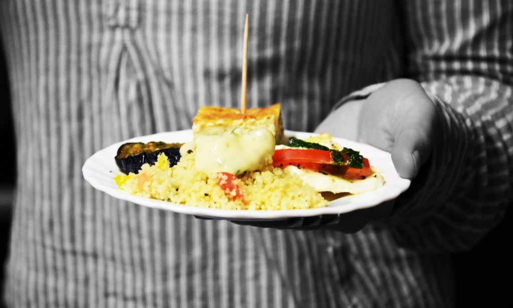 Die Grafik zeigt den Torso einer Person in schwarz-weiß, der Teller mit Häppchen, den die Person hält erstrahlt in knalligen Farben.