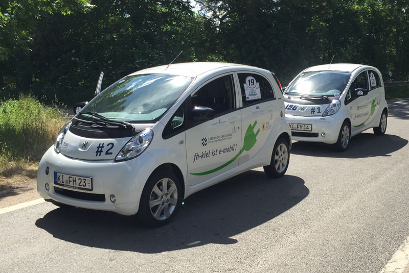 Zwei E-Autos stehen hintereinander an einer Ladesäule.