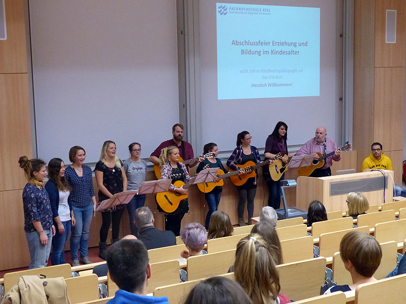 Eine Gruppe Musizierender steht mit Gitarren und Instrumenten in einem Hörsaal.