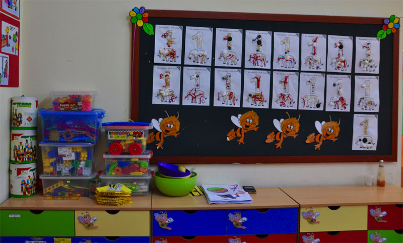 An einer Wand hängt ein Holzboard mit Basteleien von Kindern. Darunter und daneben finden sich Kästen mit Spielzeug.