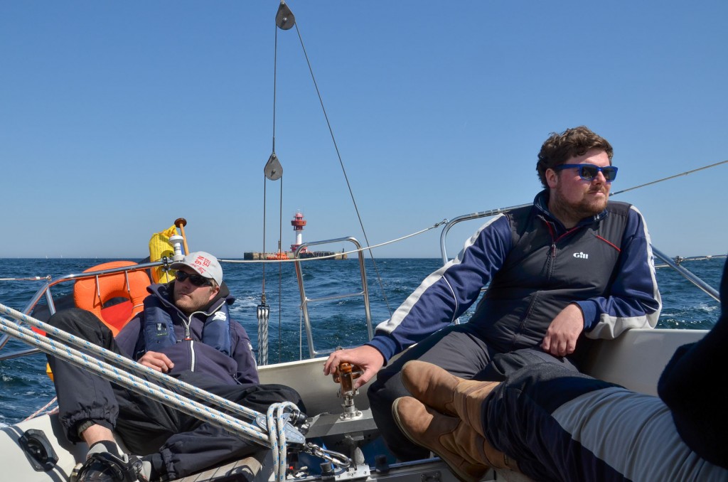 Zwei Männer sitzen entspannt am Heck eines Segelbootes und genießen die Fahrt.