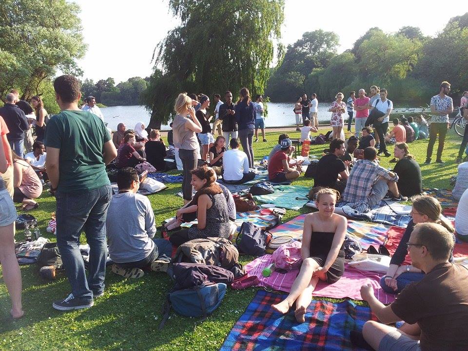 Eine kleine Menschenmenge hat es sich mit Sitzdecken in einem grünen Park gemütlich gemacht.