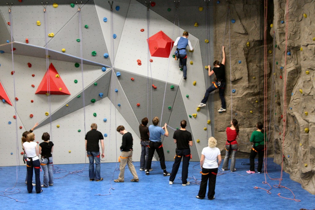 Mehrere gesicherte Paare erklimmen in Teamarbeit eine Kletterwand.