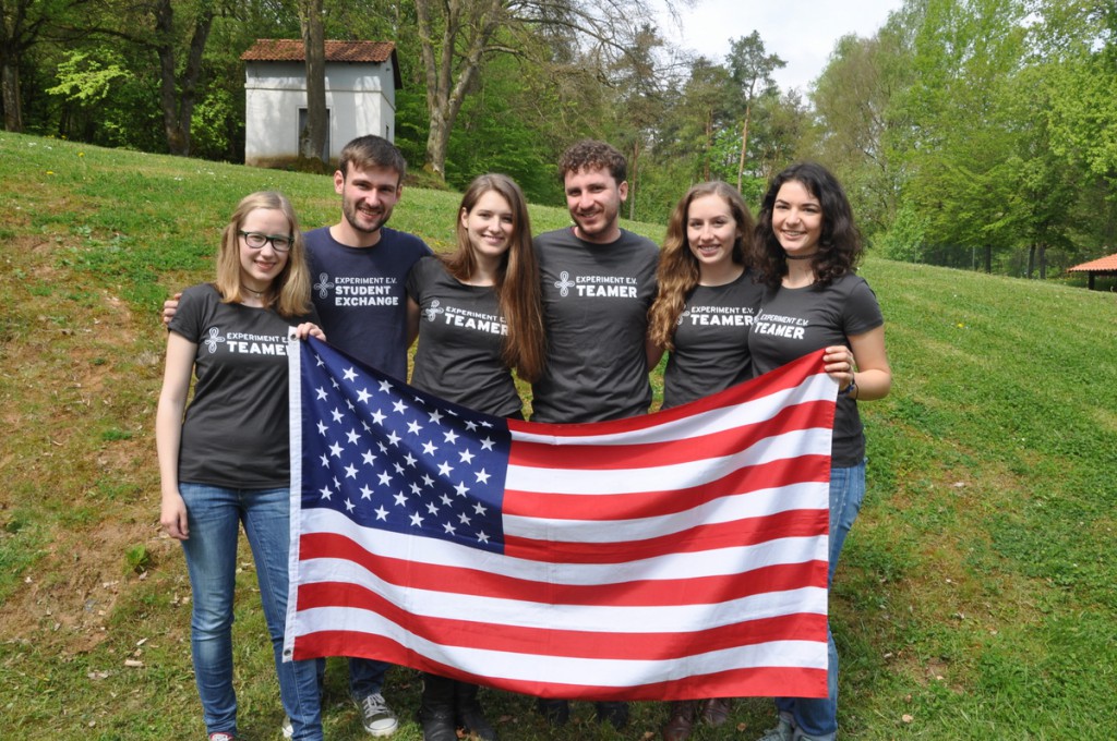 Eine Gruppe Studierender, in passenden T-Shirts, hält eine USA Flagge und posiert für die Kamera.