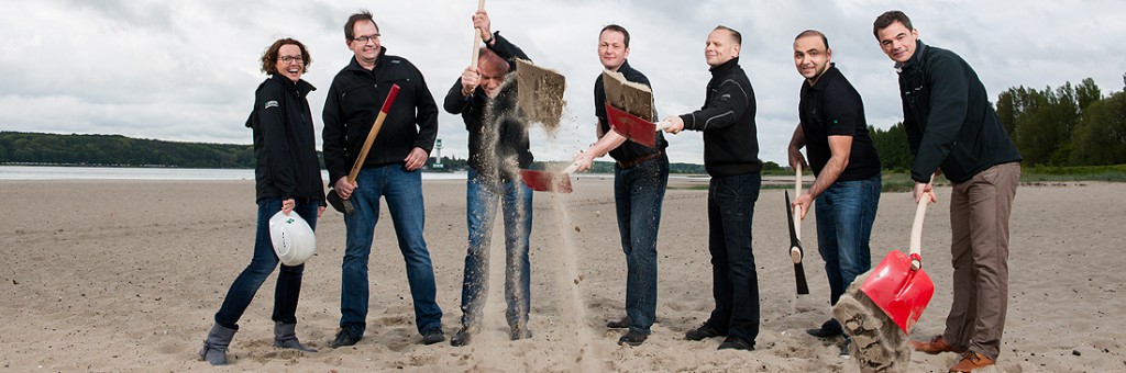 Eine Gruppe Menschen wirft Strandsand mit ihren Schaufeln hoch.