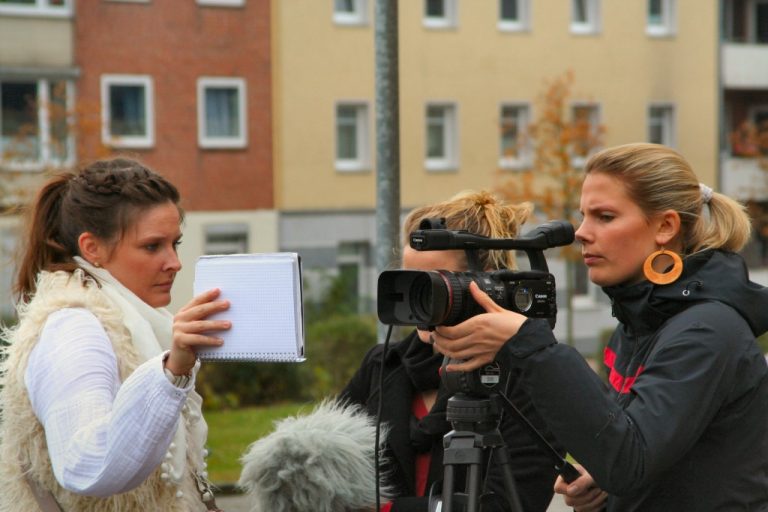Drei Frauen drehen mit einer Videokamera eine Szene.