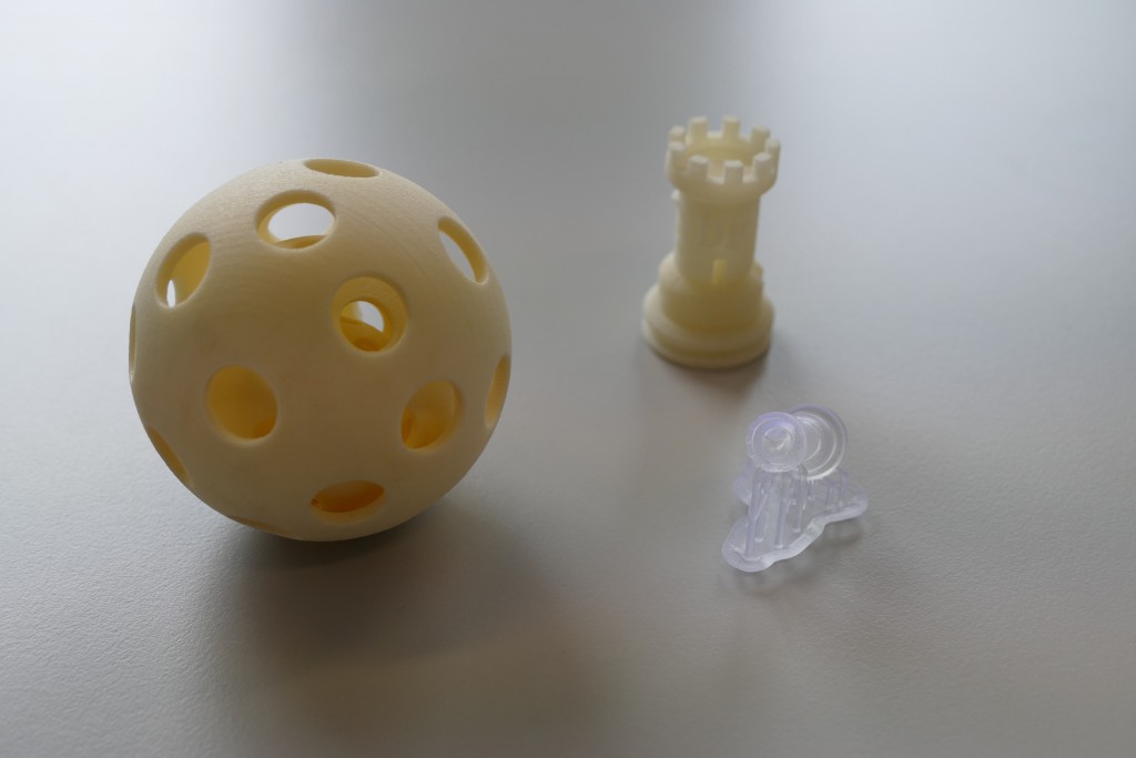 Drei aus dem 3D-Drucker stammende  Gegenstände. Zwei von ihnen sind eher gelblich, einer von ihnen ist nahe zu weiss-transparent.