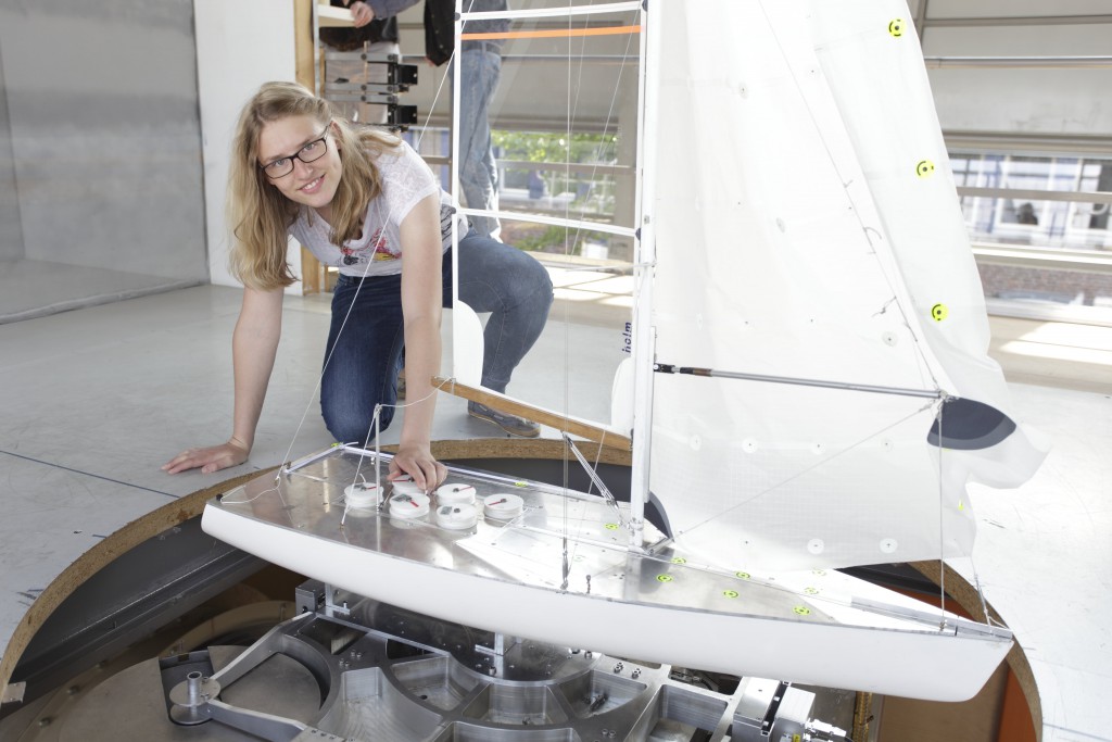 Eine Frau stellt etwas an einer Segelbootsimualtionskonstruktion ein und lächelt in die Kamera.