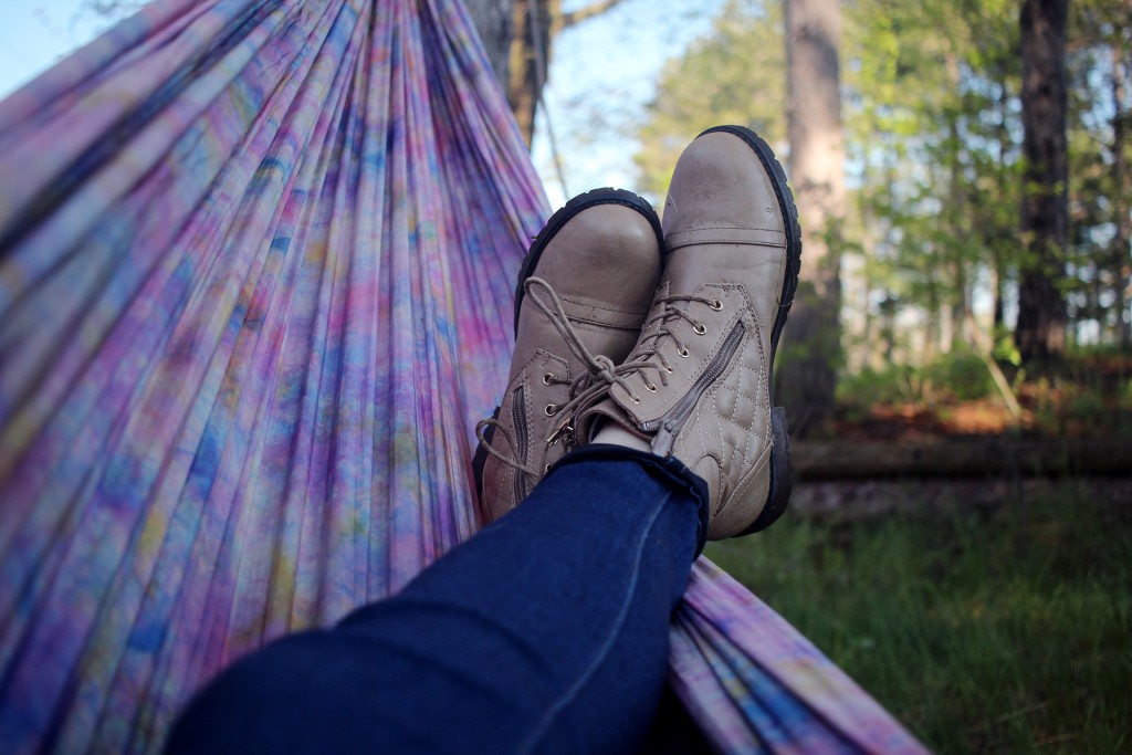 Zwei mit Stiefeln bekleidete Füße liegen in einer lilanen Hängematte im Freien.