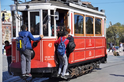 Drei Jungen halten sich außen an einer Straßenbahn fest.