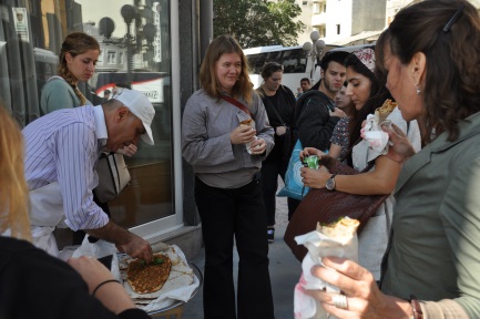 Eine Gruppe Studentinnen kauft etwas zu Essen bei einem Straßenhändler.