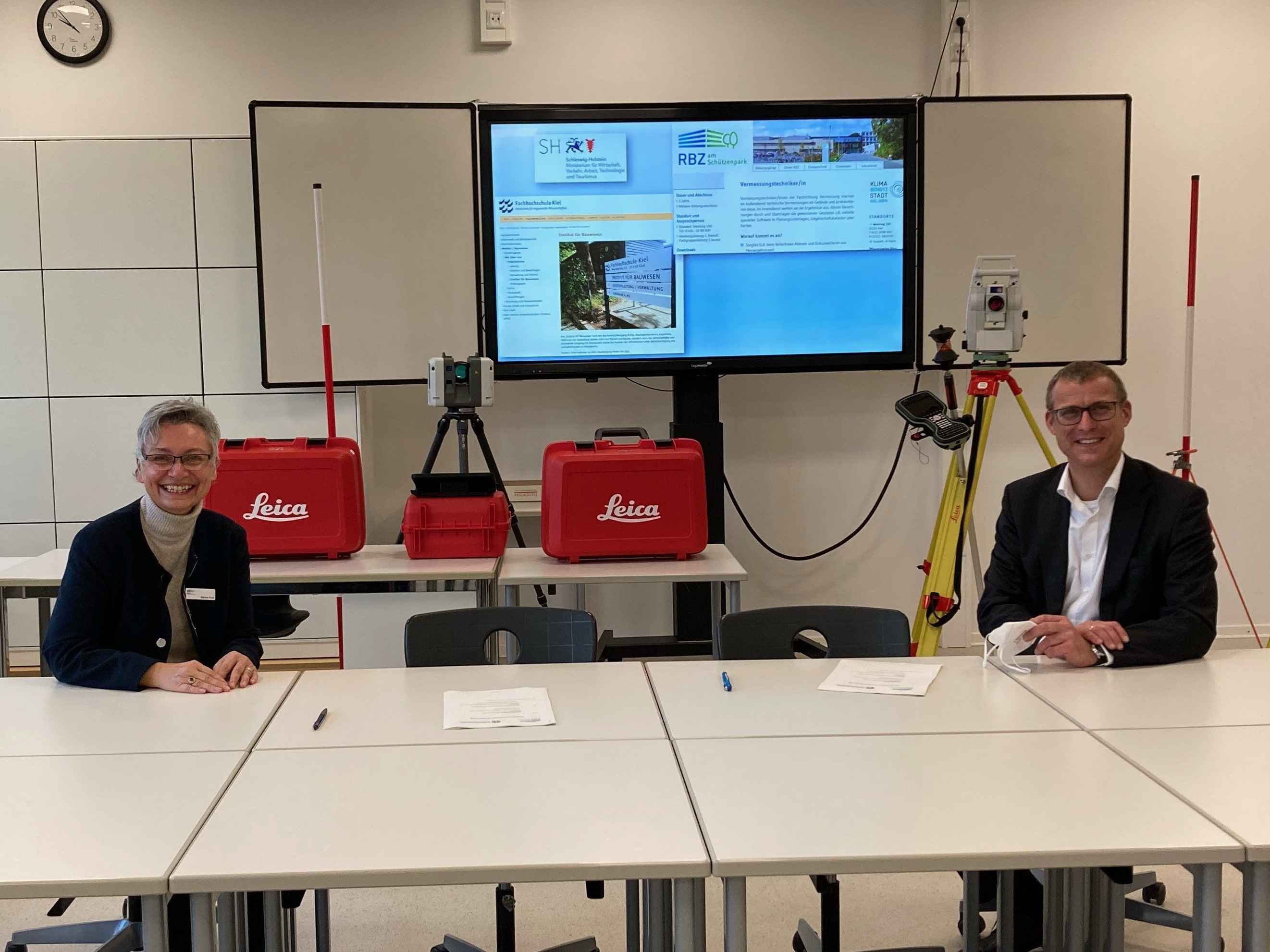 Martina Propf, Schulleiterin RBZ am Schützenpark und Prof. Dr. Björn Christensen, Präsident der FH Kiel, sitzen an einem TIsch mit Abstand und lächeln in die Kamera. Foto: ©SHIBB/Lucks. 